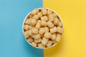 Close up of Cheese Potato Puff Snacks ball and buds, Popular Ready to eat crunchy and puffed snacks buds, cheesy salty pale-yellow color over blue yellow background - obrazy, fototapety, plakaty
