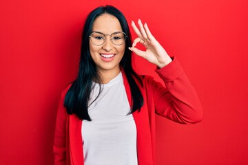 Beautiful hispanic woman with nose piercing wearing casual look and glasses smiling positive doing ok sign with hand and fingers. successful expression.