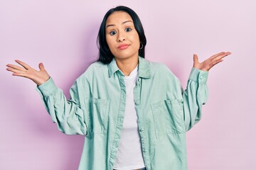 Beautiful hispanic woman with nose piercing wearing casual green jacket clueless and confused with open arms, no idea and doubtful face.