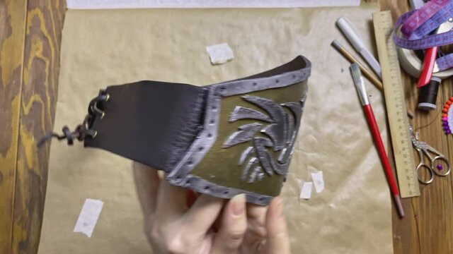 Corset with dragon from eva foam in women's hands. Detail of viking or celtic costume with leather belt and lacing. Cosplayer workshop. Sheet of craft paper on wooden table.