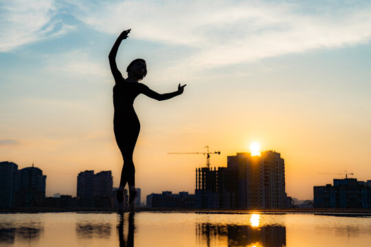 Silhouette of ballerina performing on cityscape and dramatic sunset background. Concept of tenderness, lightness, airiness