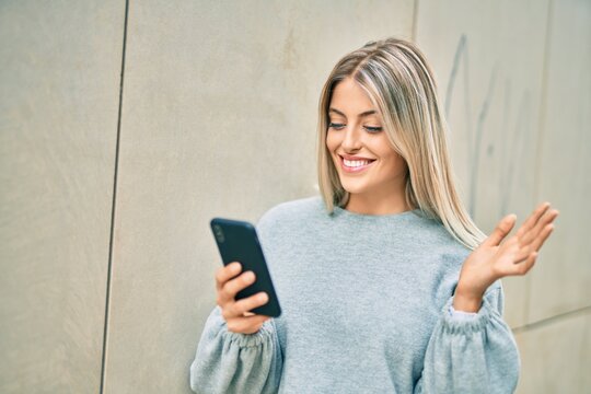 Young blonde girl smiling happy doing video call using smartphone at the city