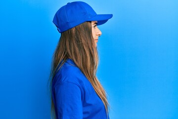 Young hispanic woman wearing delivery uniform and cap looking to side, relax profile pose with natural face with confident smile.