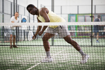 Focused African American playing friendly paddleball match on small closed court. Concept of...