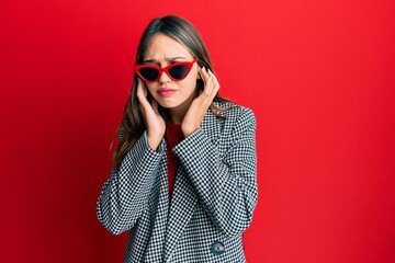 Fototapeta premium Young brunette woman wearing fashion and modern look covering ears with fingers with annoyed expression for the noise of loud music. deaf concept.