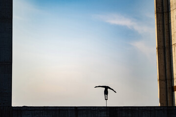 Silhouette of flexible girl dong handstand in split on sky background. Concept of individuality,...
