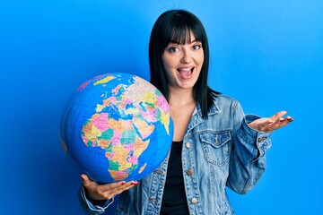 Young hispanic woman holding world ball celebrating achievement with happy smile and winner expression with raised hand