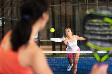 Positive attractive female player hits the ball while playing padel