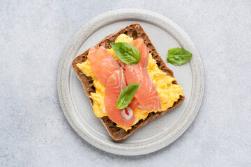 Breakfast toast with scrambled eggs and smoked salmon Lox on grey plate, top view. Isolated on grey concrete background. Tasty healthy sandwich with egg and salmon