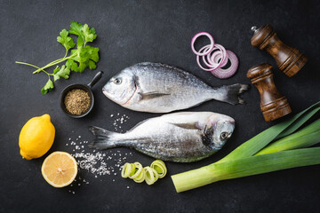 Uncooked dorado fish, spices and vegetables on a black slate concrete background. Top view. Cooking healthy dinner food concept, flat lay composition