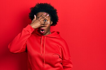 Fototapeta na wymiar Young african american woman wearing casual sweatshirt peeking in shock covering face and eyes with hand, looking through fingers with embarrassed expression.