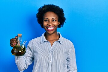 Young african american woman holding olive oil can looking positive and happy standing and smiling...