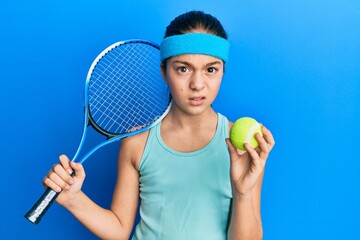 Beautiful brunette little girl playing tennis holding racket and ball skeptic and nervous, frowning upset because of problem. negative person.