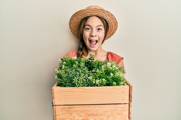 Beautiful brunette little girl wearing gardener hat holding wooden plant pot celebrating crazy and amazed for success with open eyes screaming excited.