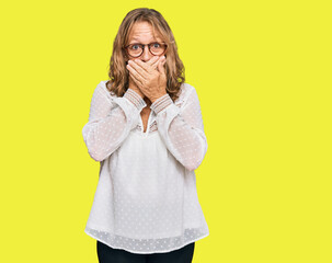 Middle age blonde woman wearing casual white shirt and glasses shocked covering mouth with hands for mistake. secret concept.