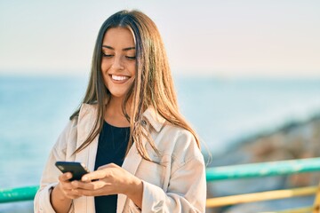 Young hispanic girl smiling happy using smartphone at the promenade.