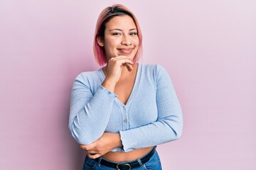 Hispanic woman with pink hair standing over pink background smiling looking confident at the camera...