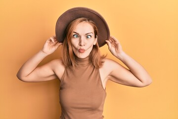 Young caucasian woman wearing hat making fish face with mouth and squinting eyes, crazy and comical.