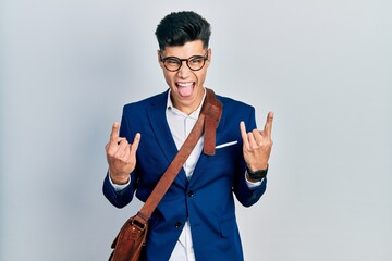 Young hispanic man wearing business clothes shouting with crazy expression doing rock symbol with hands up. music star. heavy concept.