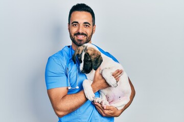 Handsome hispanic veterinary man with beard checking dog health smiling with a happy and cool smile...
