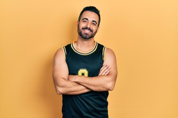 Handsome hispanic man with beard wearing basketball t shirt happy face smiling with crossed arms looking at the camera. positive person.