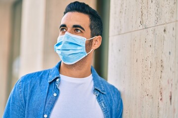 Young hispanic man wearing medical mask standing at the city.