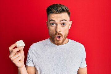 Young redhead man holding fresh garlic scared and amazed with open mouth for surprise, disbelief face
