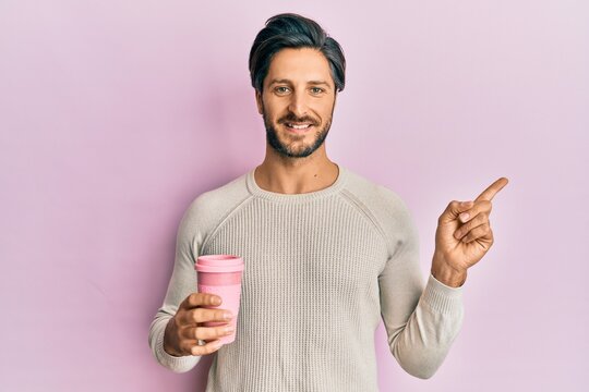 Young hispanic man drinking a take away cup of coffee smiling happy pointing with hand and finger to the side