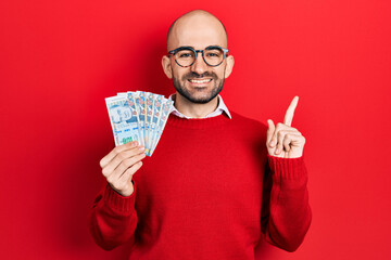 Young bald man holding peruvian sol banknotes smiling happy pointing with hand and finger to the side