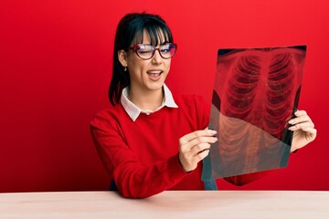 Young brunette woman with bangs holding chest radiography winking looking at the camera with sexy...