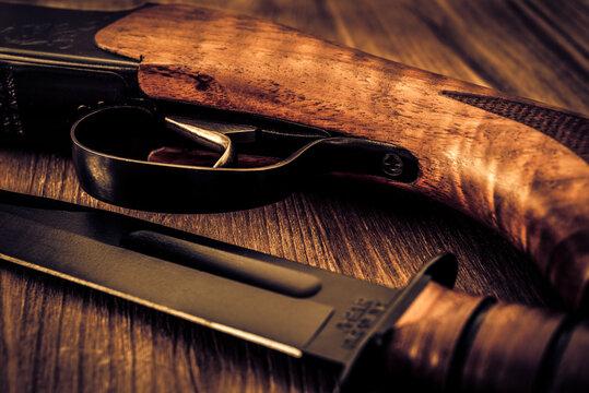 Hunting rifle with combat knife lying on a wooden table