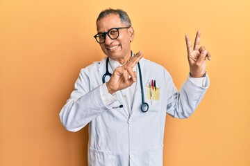 Middle age indian man wearing doctor coat and stethoscope smiling looking to the camera showing...