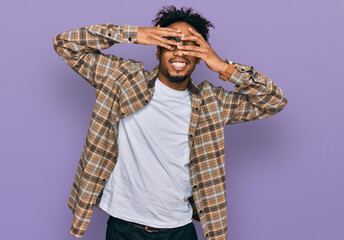 Young african american man with beard wearing casual clothes and glasses covering eyes with hands smiling cheerful and funny. blind concept.