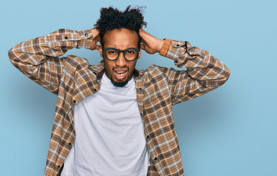 Young african american man with beard wearing casual clothes and glasses crazy and scared with hands on head, afraid and surprised of shock with open mouth