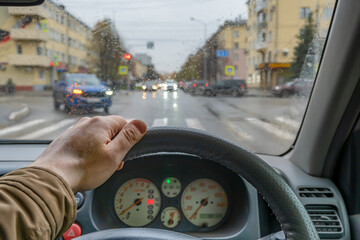 driver hand on the steering wheel inside the car while parking at a traffic light in front of a...
