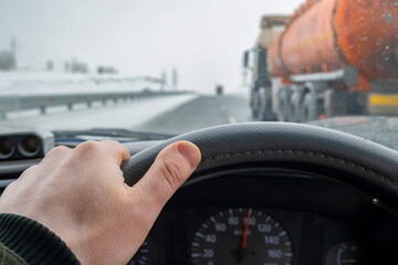 driver hand on the steering wheel inside the car while overtaking on the left lane of a tanker truck with a tank of dangerous flammable, combustible cargo, gasoline, diesel fuel