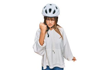 Teenager caucasian girl wearing bike helmet angry and mad raising fist frustrated and furious while shouting with anger. rage and aggressive concept.