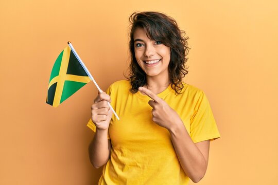 Young hispanic woman holding jamaica flag smiling happy pointing with hand and finger