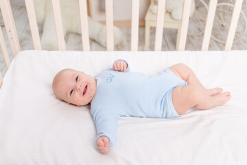 baby in the crib, cute little boy of six months lying in the nursery on the bed