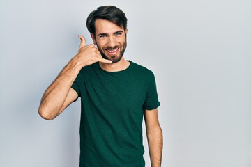 Young hispanic man wearing casual white tshirt smiling doing phone gesture with hand and fingers like talking on the telephone. communicating concepts.