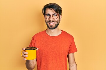 Young hispanic man drinking a cup of coffee looking positive and happy standing and smiling with a confident smile showing teeth