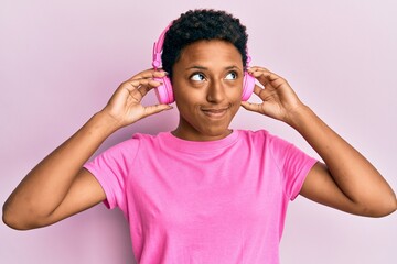 Young african american girl listening to music using headphones smiling looking to the side and staring away thinking.