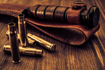 Obraz premium Empty shells from the rifle and leather sheath with combat knife lying on a wooden table. Focus on the shells