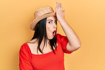 Young hispanic woman wearing summer hat surprised with hand on head for mistake, remember error....