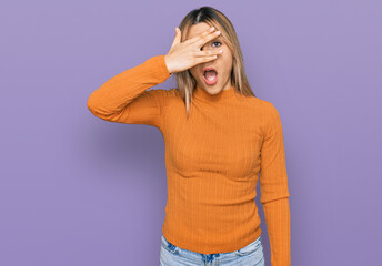 Young caucasian woman wearing casual clothes peeking in shock covering face and eyes with hand, looking through fingers with embarrassed expression.