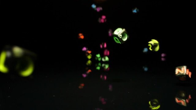 Multi-colored letter beads fall on to mirror in slow motion.