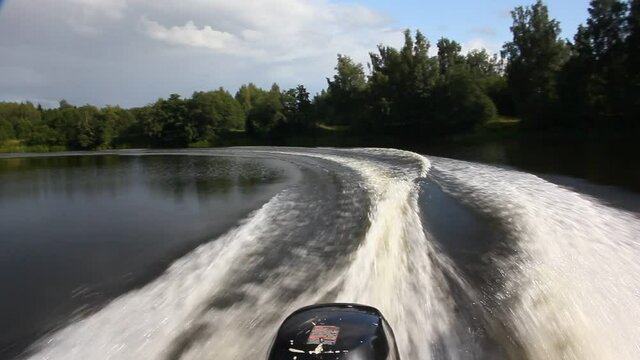 Speedboat turn on the small river water with circle keelwater trail on green dark shores background at summer day, rear view on foamy transom wake from stern of motor boat with single outboard motor