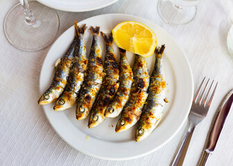 Malaga cuisine grilled sardines served with lemon on white plate on wooden table