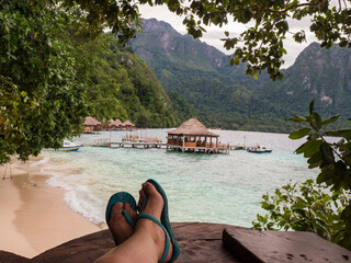 Ora Beach, Indonesia - Feb, 2018: Relax over the turquoise water. Woman feet over the wooden pond....