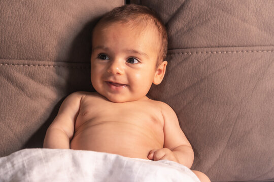 Two month old Caucasian baby sitting on a sofa smiling looking at camera. Newborn studio photos